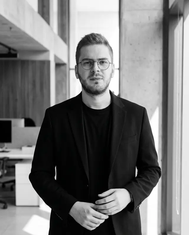 Ali Sarraj, CEO of Daut Labz, wearing round glasses and a black blazer in a concrete-and-glass office.